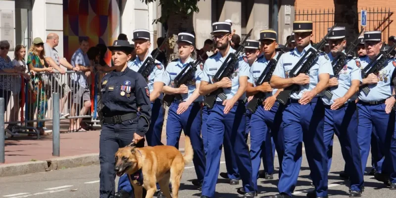 Défilé militaire de gendarmes en uniforme bleu, encadrés par une femme officier accompagnée d’un chien, illustrant le rôle de l’officier de gendarmerie dans le commandement opérationnel et les missions de sécurité publique.
